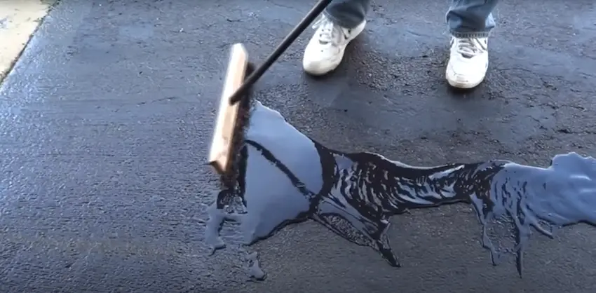 Close-up of driveway sealer being spread on an asphalt surface with a squeegee