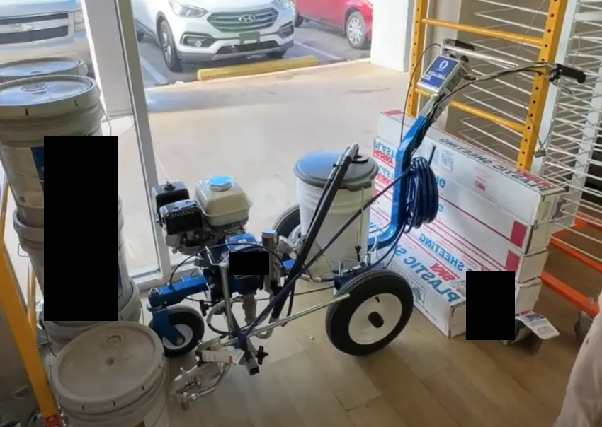 Striping machine with white paint ready for use, displayed indoors next to paint supplies