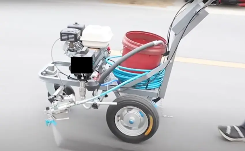 Striping machine being used to apply white lines on pavement in a parking lot