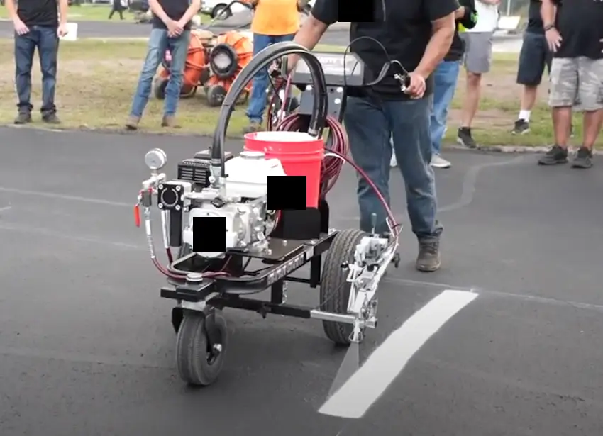 Close-up of a professional-grade striping machine applying thick white lines on asphalt