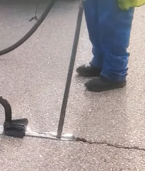 Worker performing crack sealing on asphalt pavement, using a sealing tool