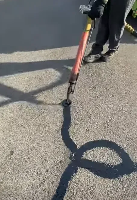 Worker sealing cracks on asphalt pavement with precision tools