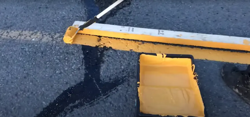 Applying yellow striping on asphalt with a roller for parking lot lines