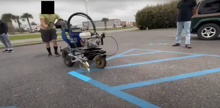 Machine painting blue striping on a parking lot for accessibility spaces