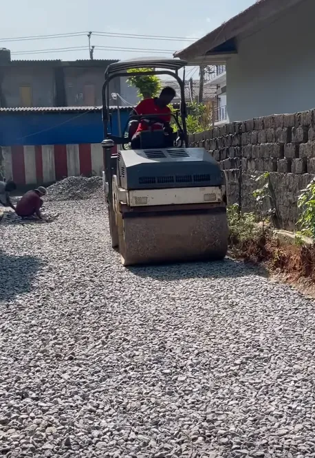 Worker operating a compactor to compress crushed stone on a macadam road surface.