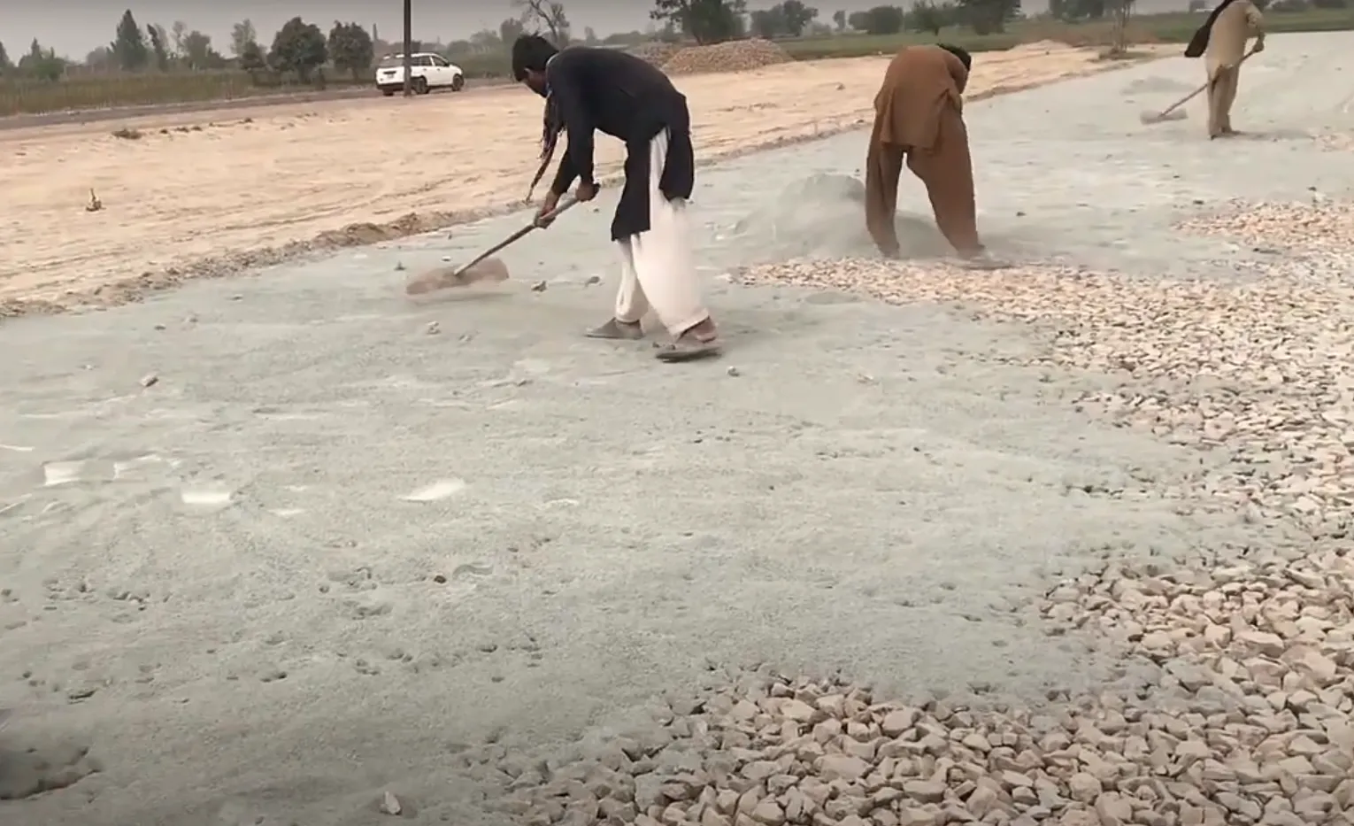 Two workers spreading gravel on a road surface during macadam road construction.