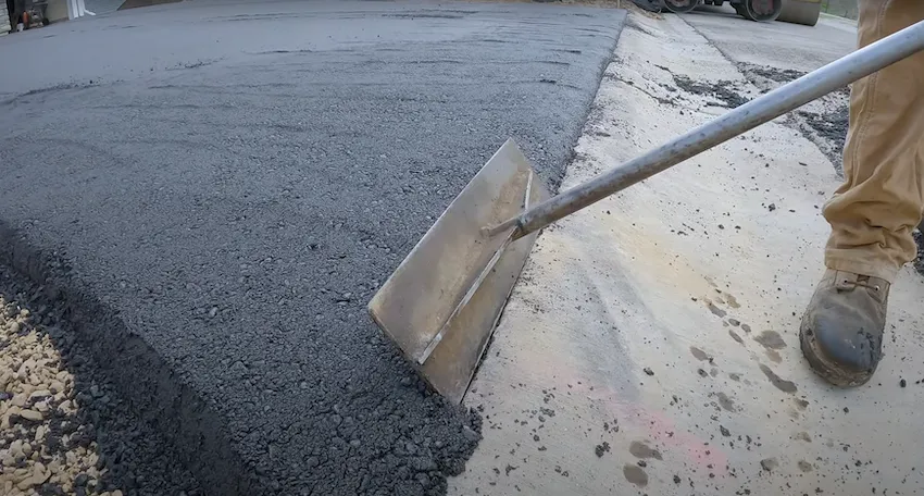 Close-up of a worker using a tool to spread and level asphalt on a driveway.