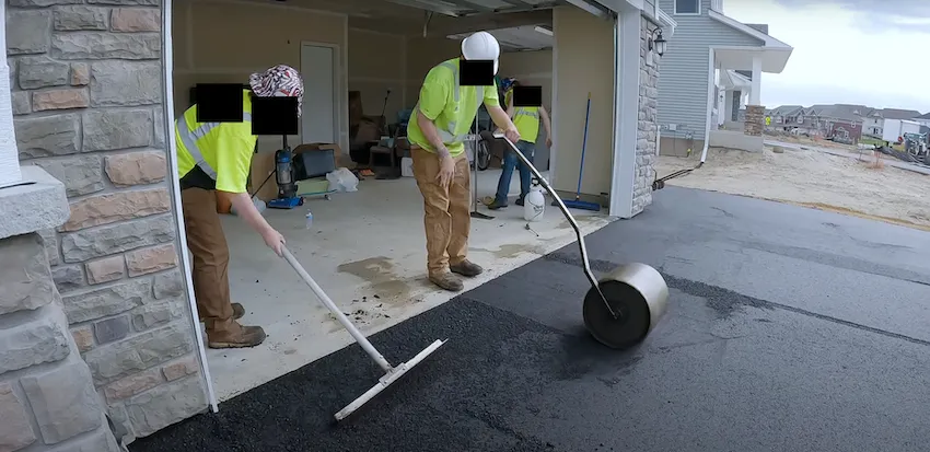 Workers compacting and smoothing asphalt at the entrance of a residential garage.