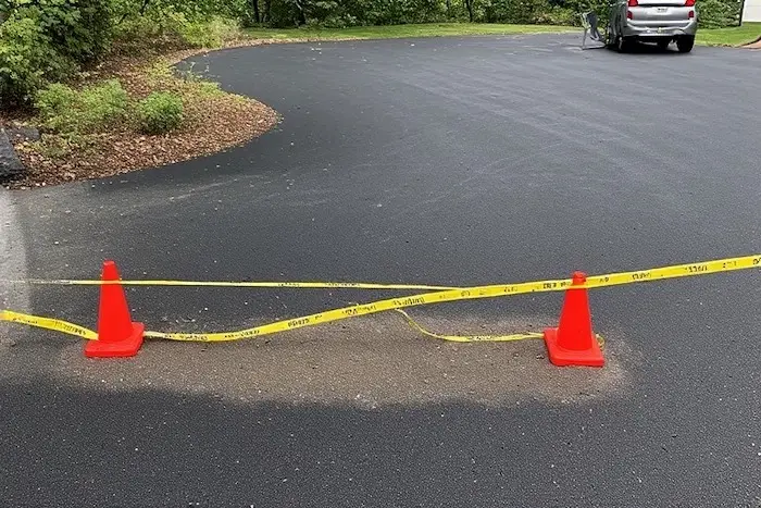 Allée en asphalte fraîchement scellée avec des barrières temporaires et un ruban de signalisation pour empêcher l'accès