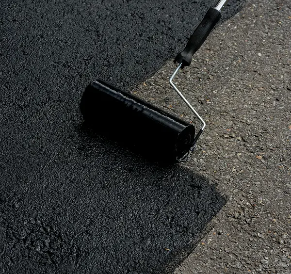 Application d'un scellant acrylique sur une petite surface d'asphalte avec un rouleau, montrant la finition brillante