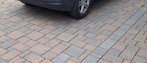 Vue en gros plan d'une allée résidentielle pavée avec des pavés imbriqués, présentant un design propre et durable avec une voiture garée dessus.