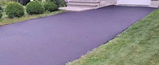 Une allée en asphalte lisse menant à l'entrée d'une maison résidentielle, bordée par une pelouse bien entretenue.