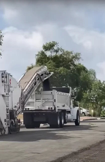 Une grande fraiseuse blanche équipée d'un tapis roulant charge de l'asphalte recyclé à l'arrière d'un camion-benne.