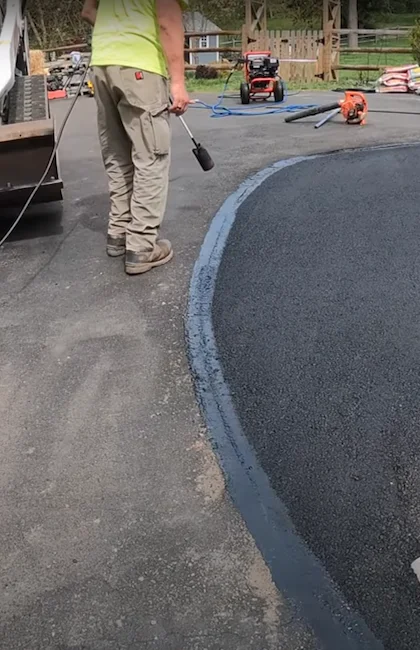 Un ouvrier utilise un chalumeau pour chauffer les bords d'une surface d'asphalte fraîchement posée afin de créer un joint lisse.